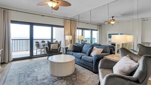 Een ruime woonkamer met een grote bank, fauteuils, een salontafel en een balkon met uitzicht.