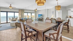 Een ruime eethoek met een houten tafel en stoelen, een plafondventilator en een groot raam met uitzicht op de oceaan.