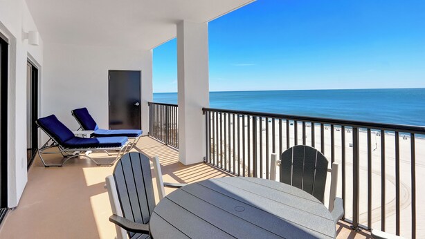 Een balkon met een tafel en stoelen, uitkijkend op een strand.