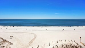 Een breed zandstrand met een helderblauwe lucht en rustige zee.