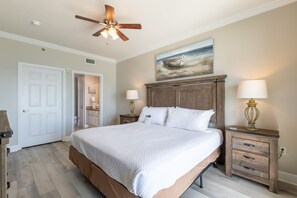 A bedroom with a large bed, wooden headboard, two bedside tables with lamps, a ceiling fan, and a painting of a boat on the wall. - Seawind 1105 by Liquid Life (Gulf Shores)