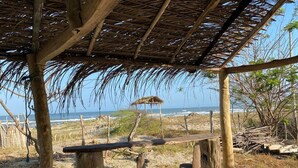 En trækonstruktion med stråtækt tag, en bænk og udsigt over havet.