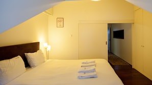 A hotel room with a bed, a nightstand with lamps, a framed picture on the wall, and a door leading to another room.
