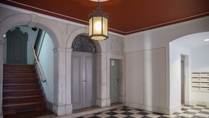 A hallway with a checkered floor, a staircase with a wooden handrail, and a light fixture above.