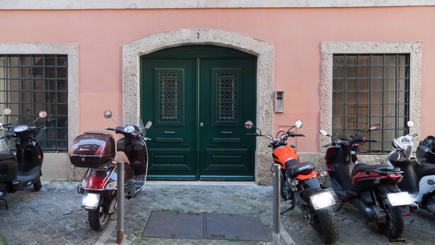 A row of parked scooters in front of a building with a green door and a stone archway.