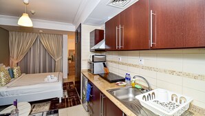 Een kleine hotelkamer met kitchenette, een bed met gordijnen, een tafeltje met een kaars en uitzicht op buiten.