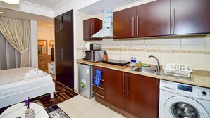 Een compacte hotelkamer met een bed, een kitchenette, een wasmachine en een badkamer.