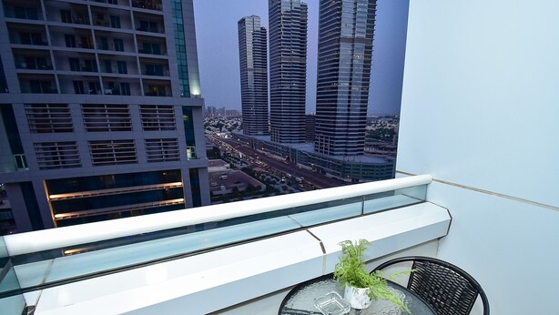 Een balkon met een glazen hekwerk, een ronde glazen tafel met een bloempot en twee zwarte stoelen.