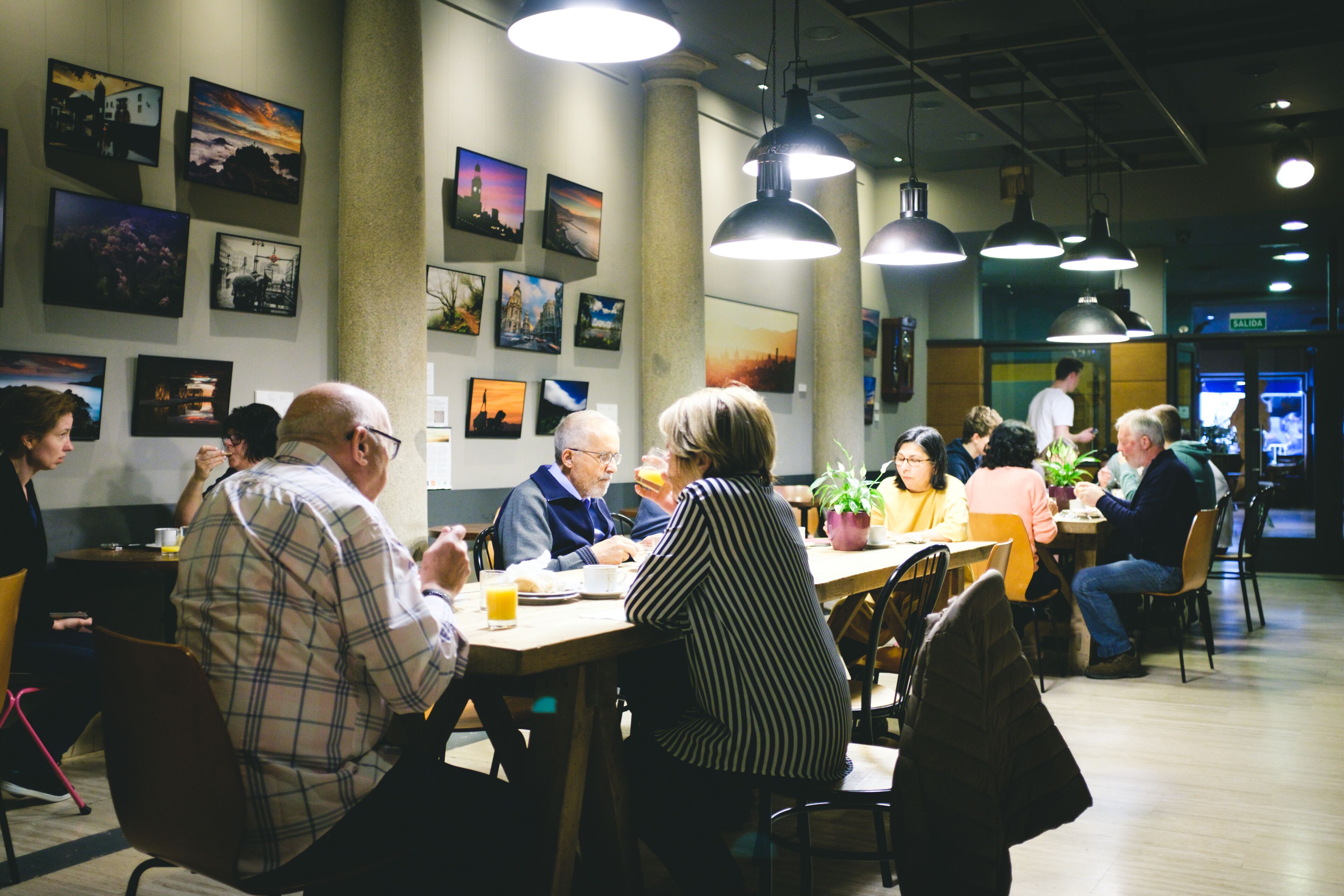 Een eetruimte met tafels en stoelen, mensen aan het eten, en kunstwerken aan de muren.