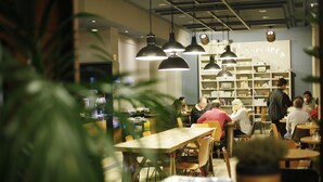 A cafe with wooden tables and chairs, hanging pendant lights, and a bookshelf in the background. - Hostal Persal (Madrid)
