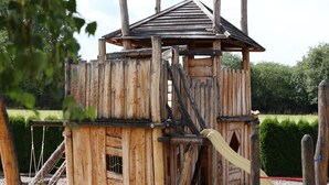 A wooden play structure with a slide and climbing elements, surrounded by gravel and greenery. - Cottages Oberdorla at the center here in Germany Thüringen (Oberdorla)
