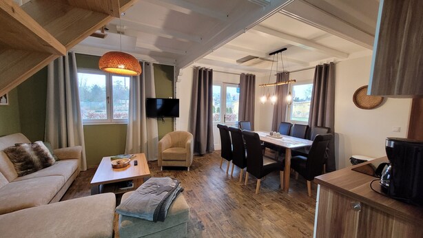 A spacious living area with a sofa, ottoman, dining table, chairs, and a television. - Cottages Oberdorla at the center here in Germany Thüringen (Oberdorla)