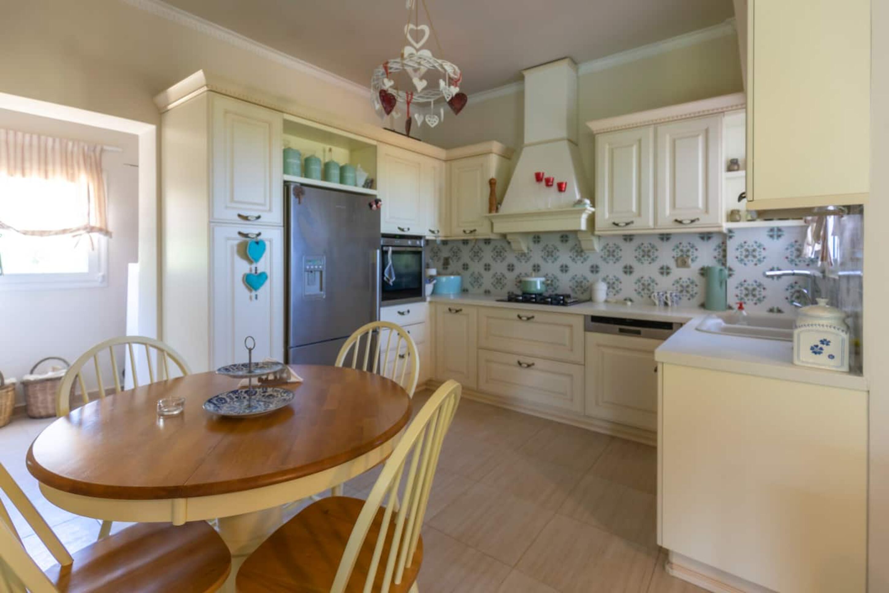 A kitchen with white cabinets, a wooden dining table, and a chandelier.