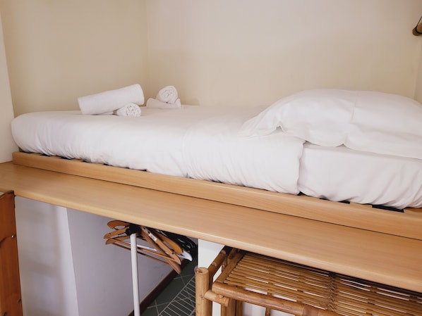 Ein Einzelbett mit weißer Bettwäsche, einem Holz-Kopfteil und einem kleinen Holzhocker darunter.