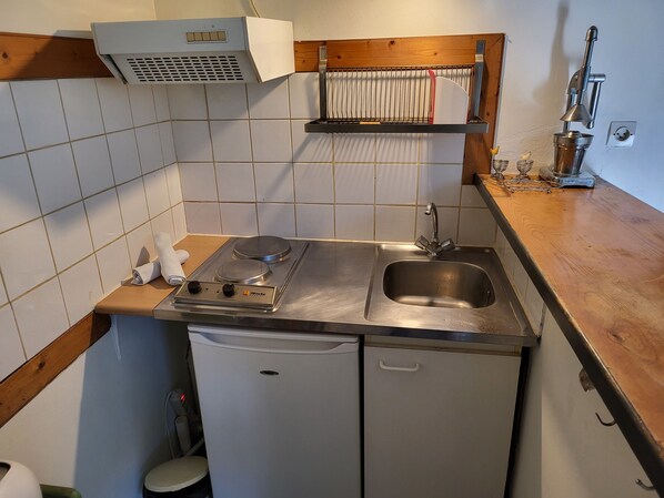 Pieni, käytännöllinen keittiö, jossa on liesi, pesuallas ja pieni jääkaappi.