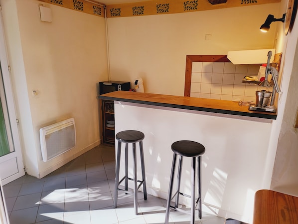 A compact kitchen with a wooden countertop, two stools, a built-in oven, and a small sink.