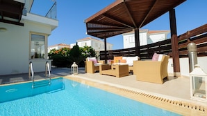 Zona de piscina con un pérgola de madera, sillones de descanso y vistas a casas vecinas.