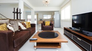 Una sala de estar moderna con un sofá marrón, una mesa de centro de madera, un sillón de cuero y un televisor sobre un mueble de madera.