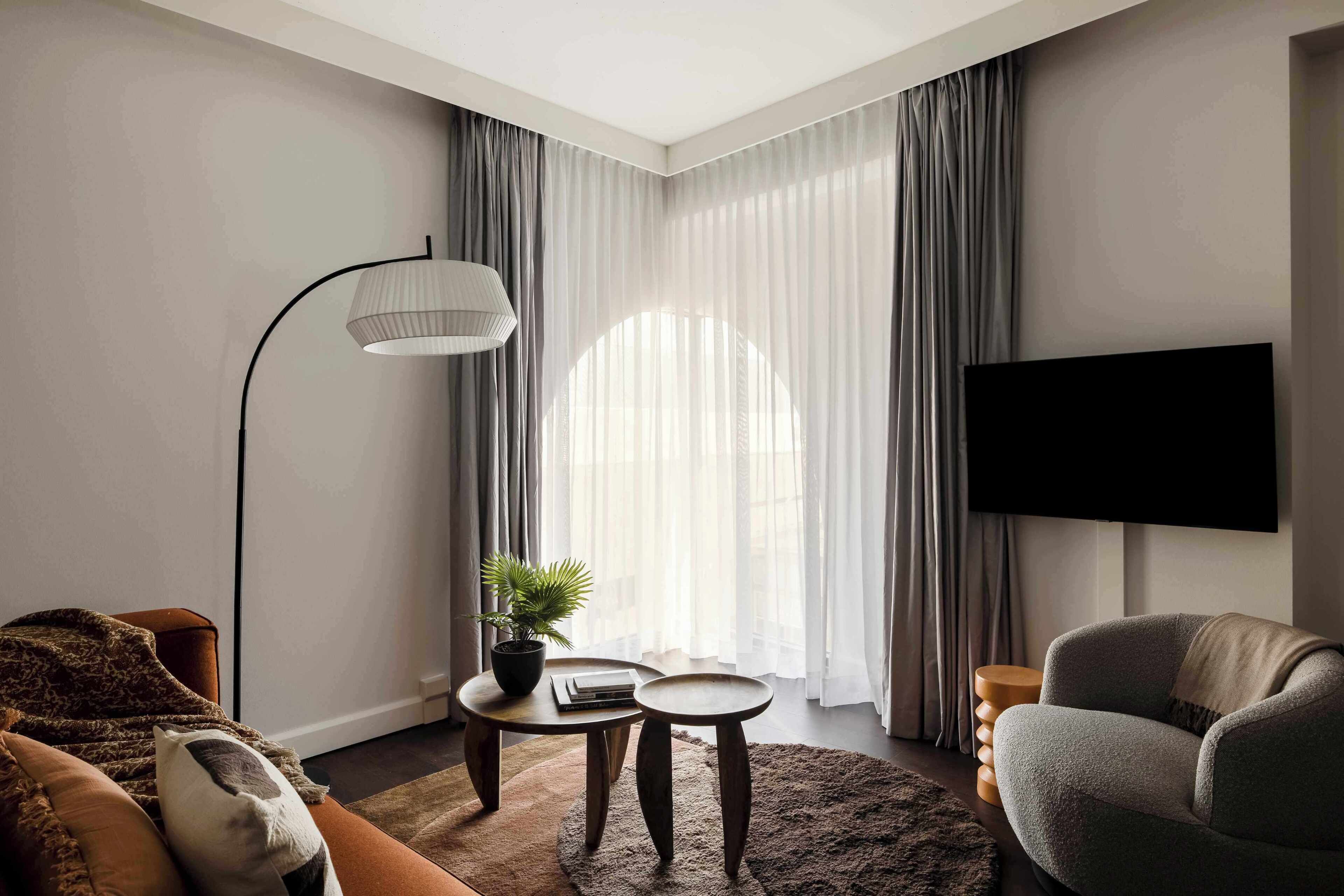 A modern living room with a sofa, a coffee table, a floor lamp, a TV, and a large window with curtains.