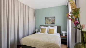 Een hotelkamer met een bed, nachtkastje, lamp, schilderij aan de muur en een vaas met bloemen.