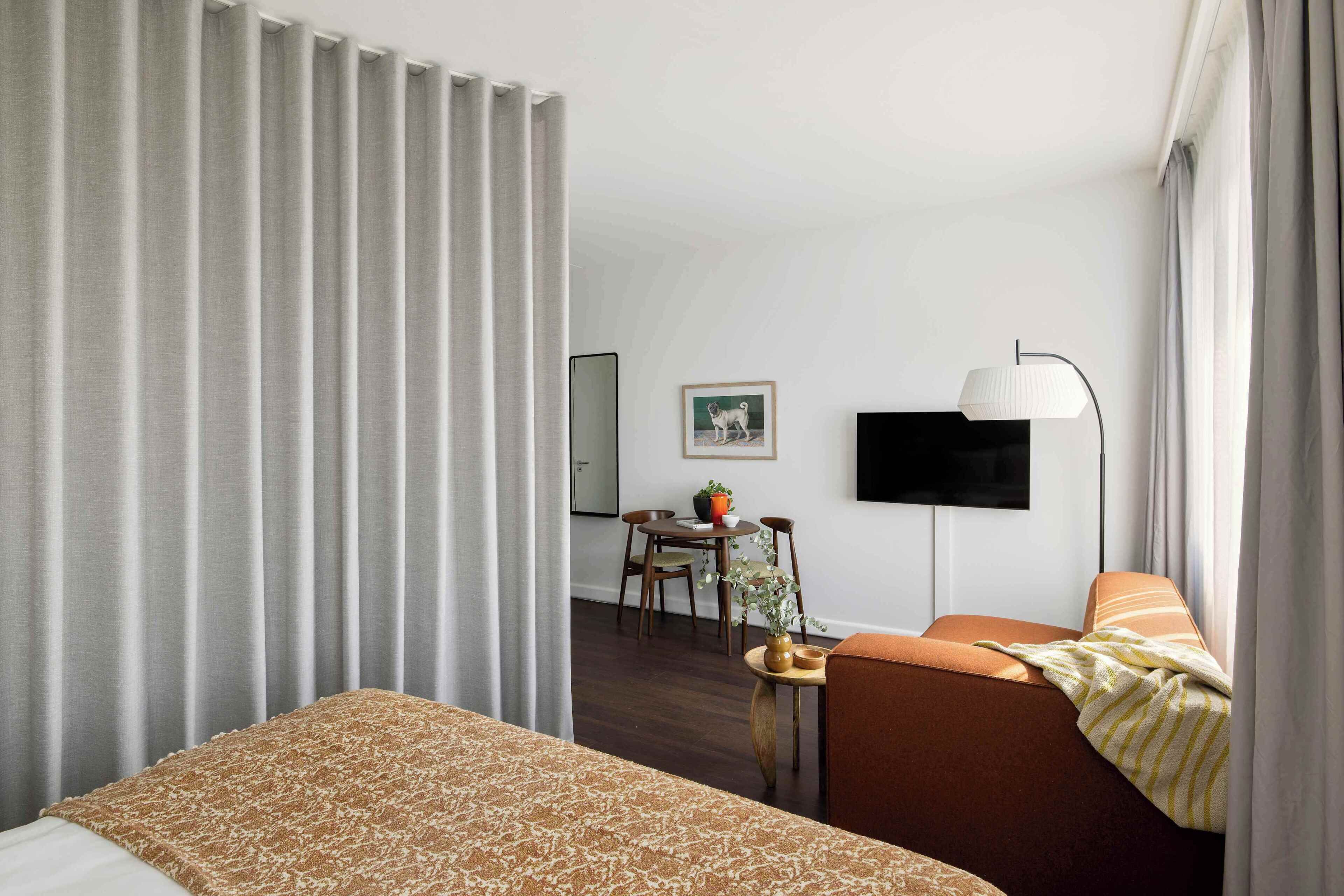 A hotel room with a bed, a sofa, a small table with a plant, a TV, and a window with curtains.