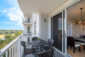 A balcony with a table and chairs, a potted plant, and a view of a green landscape.