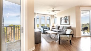 A spacious living room with a balcony, a ceiling fan, and a large window offering a view of the outdoors. - Balcony ~ Picturesque Windows ~ Outdoor Seating (Miramar Beach)