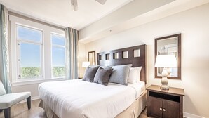A hotel room with a large bed, a nightstand, a bench, and a window with curtains. - Balcony ~ Picturesque Windows ~ Outdoor Seating (Miramar Beach)