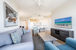A modern living room with a grey sofa, blue armchairs, a wooden coffee table, and a TV on a wooden cabinet. - Balcony ~ Picturesque Windows ~ Outdoor Seating (Miramar Beach)