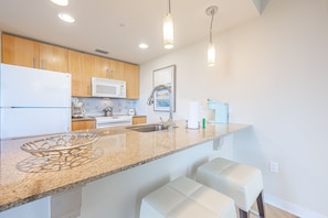 A modern kitchen with wooden cabinets, a stainless steel sink, a microwave, and a large island with bar stools. - Balcony ~ Picturesque Windows ~ Outdoor Seating (Miramar Beach)