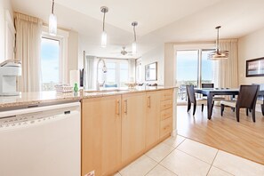 Una cocina moderna con lavavajillas, armarios de madera, zona de comedor con mesa y sillas, y ventanas amplias con vistas.
