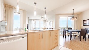 Una cocina moderna con lavavajillas, armarios de madera, zona de comedor con mesa y sillas, y ventanas amplias con vistas.