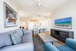 A modern living room with a grey sofa, blue armchairs, a wooden coffee table, and a TV on a wooden cabinet.