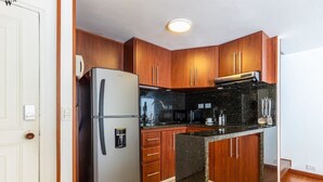 Eine moderne Küche mit Holzschränken, einem Edelstahlkühlschrank, einer Mikrowelle und einer Arbeitsplatte aus Granit.