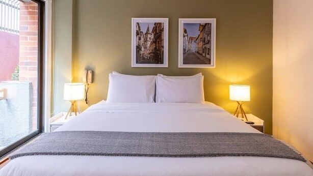Ein Hotelzimmer mit einem großen Bett, zwei Nachttischen mit Lampen und zwei gerahmten Bildern an der Wand.