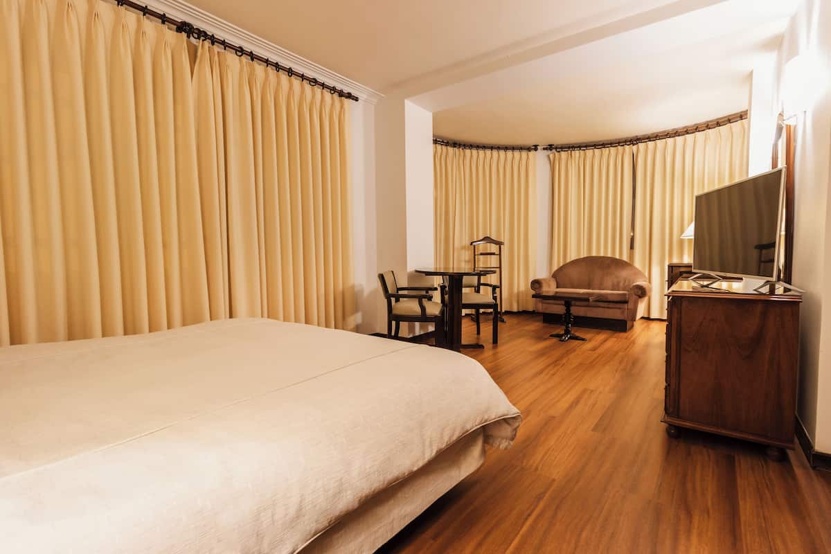 Habitación de hotel con una cama grande, un escritorio con una silla, un sofá, un televisor y cortinas.