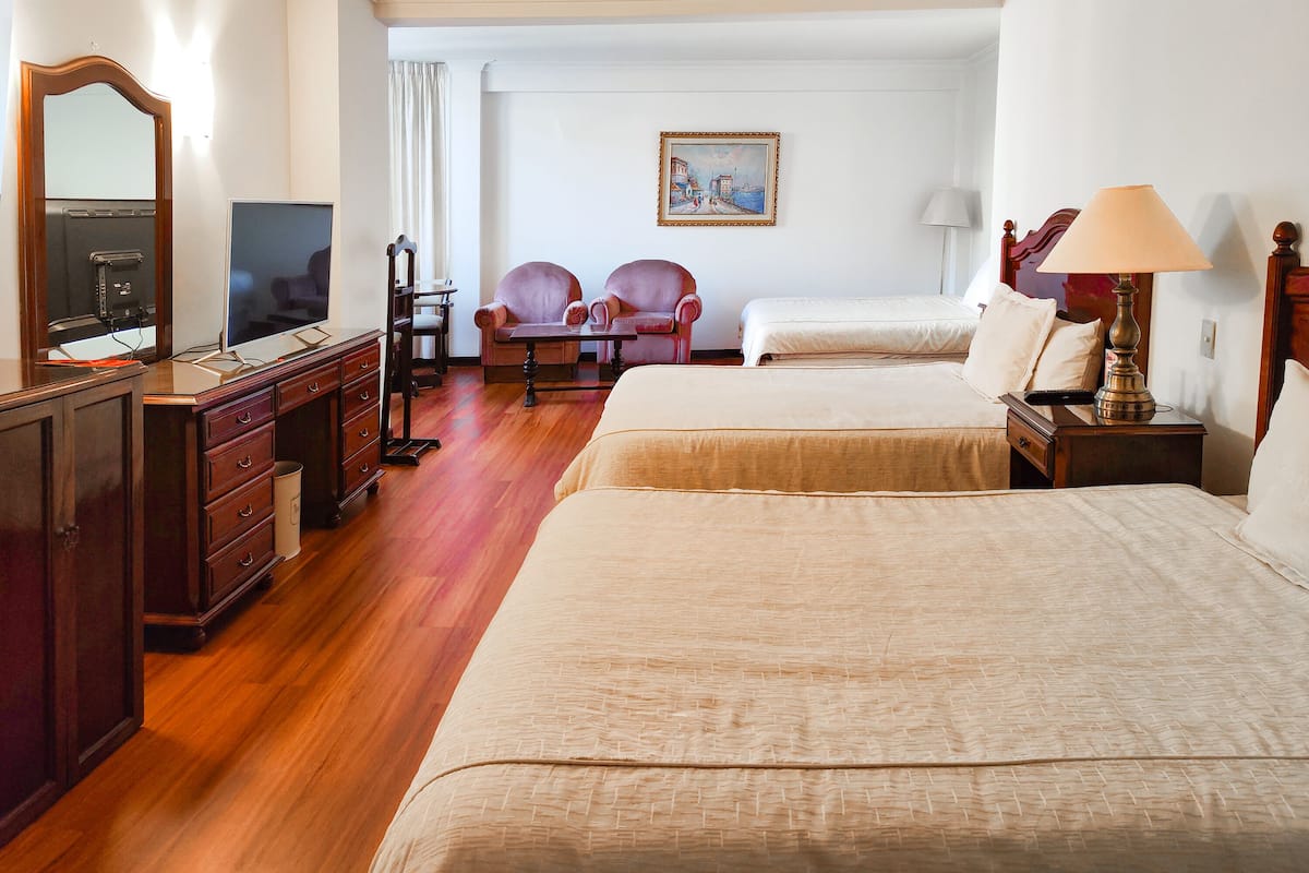 Habitación de hotel con dos camas, un escritorio con computadora, una silla, una lámpara y un cuadro en la pared.