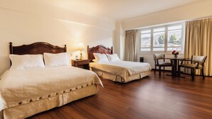 Habitación de hotel con dos camas, piso de madera, una mesa de comedor con sillas y una ventana con cortinas.
