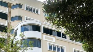 Un edificio de varios pisos con fachada curva, una entrada a nivel de calle visible con puerta de vidrio y un letrero que dice "REY PALACE".