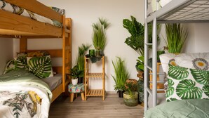 A bunk bed room with wooden headboards, a small stool, and multiple potted plants.