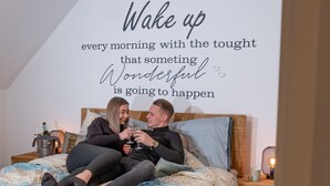 A bedroom with a bed, a bedside table, a nightstand, and a wall with a motivational quote.