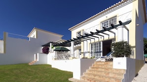 Una casa moderna de dos pisos con un porche cubierto, una escalera que conduce a la entrada y un césped bien cuidado.