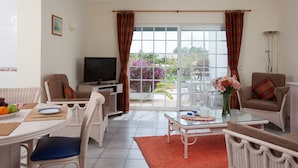 Un salón con mobiliario de mimbre, una mesa de vidrio y un televisor.