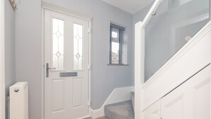 A hallway with a white door, a small window with blinds, and a staircase with a carpeted landing. - 51 Main Avenue · Luxurious Modern York House with Garden & Parking - Pass the Keys (York)