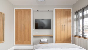 A bedroom with a bed, a TV, wooden wardrobes, a small stool, and a window with blinds. - 51 Main Avenue · Luxurious Modern York House with Garden & Parking - Pass the Keys (York)