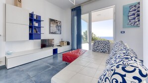 A modern living room with a sofa, a red ottoman, a bookshelf, and a flat-screen TV. - Superb villa with pool and 180° sea view (Torre Pali)
