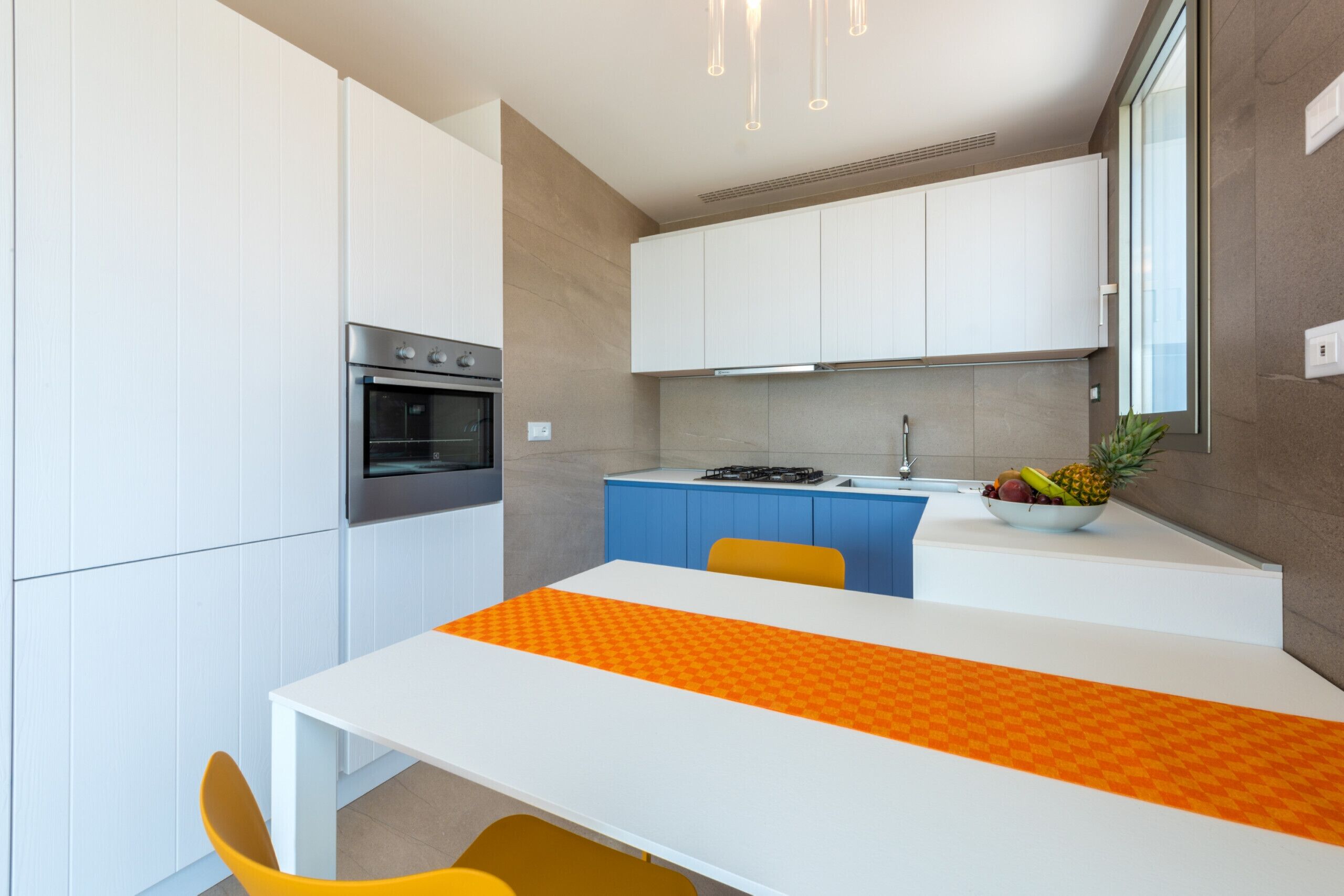 Una cocina moderna con armarios blancos, horno empotrado, estufa a gas y un frutero sobre la encimera.