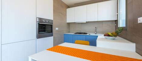 Una cocina moderna con armarios blancos, horno empotrado, estufa a gas y un frutero sobre la encimera.