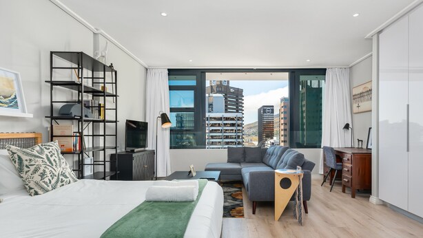 A modern hotel room with a large bed, a sofa, a desk, and a bookshelf. - 22nd Floor Apartment  With Mountain Views (Cape Town)