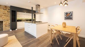 Une cuisine moderne avec des meubles blancs, un îlot central et un coin repas comprenant une table et des chaises en bois.